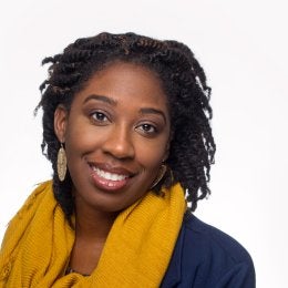 picture of African American woman smiling in a blue jacket and yellow scarf